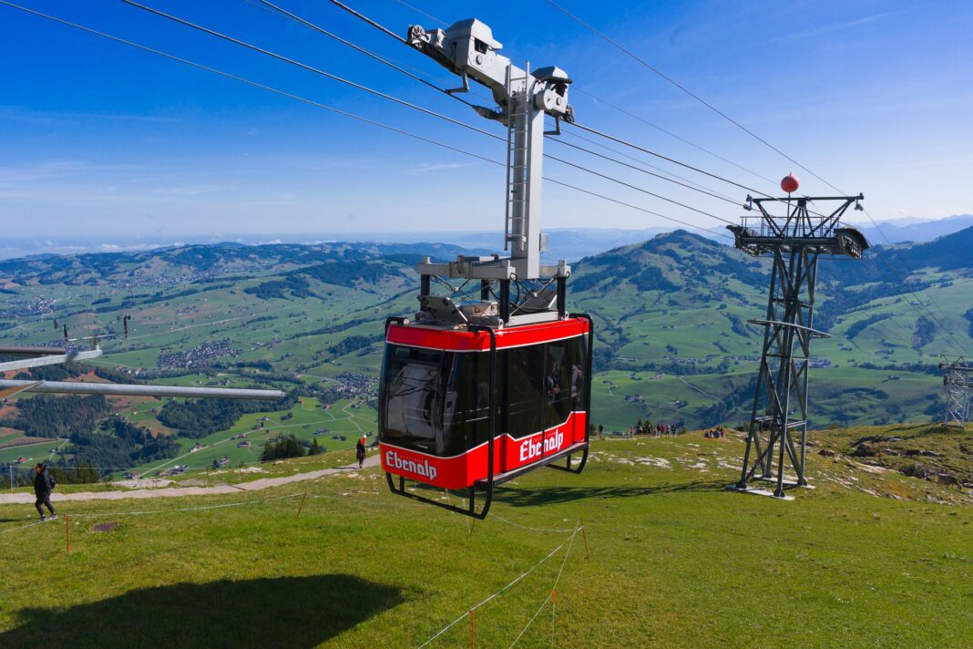 Czerwona kolejka linowa nad zielonymi krajobrazami Ebenalp w